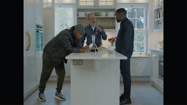 In a white, modern kitchen three men are chatting around an island unit. From the short film Mandem